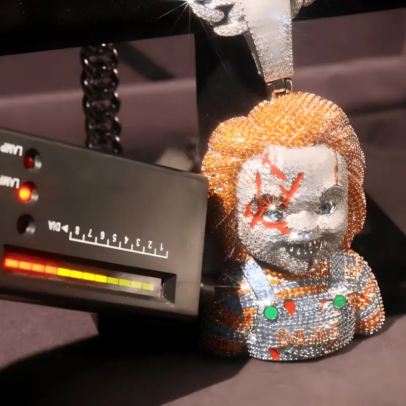A close-up of a highly embellished rhinestone keychain or pendant shaped like a horror character with orange hair, a silver face, red markings, and a silver-and-orange outfit, shown next to a black measuring device.