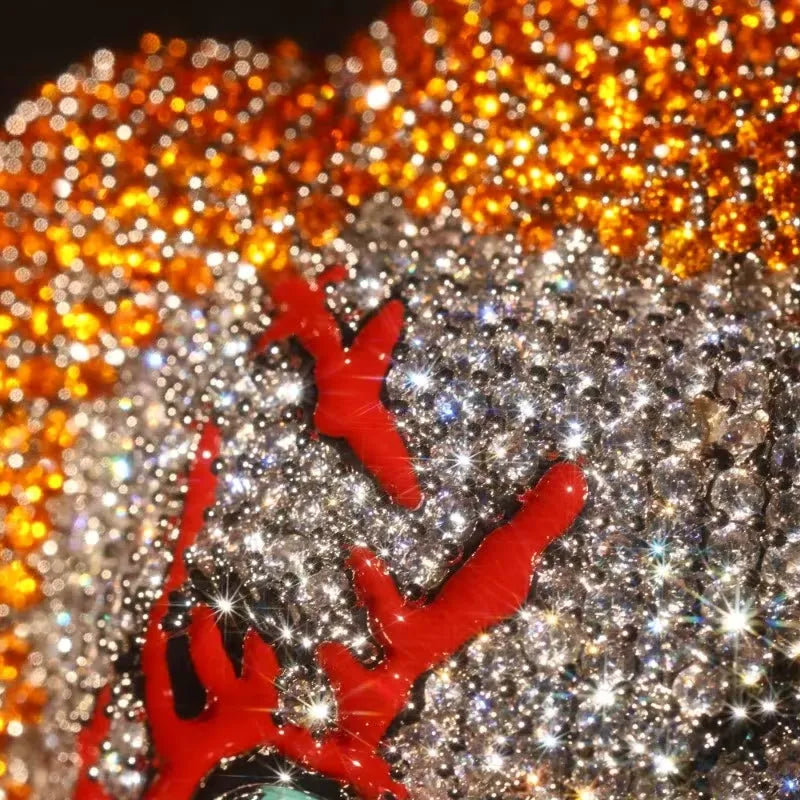 A close-up of a rhinestone-covered accessory, likely a hat or structured headpiece, featuring bright red reindeer antler shapes over a dense field of clear and silver-toned rhinestones, with a blurred orange background.