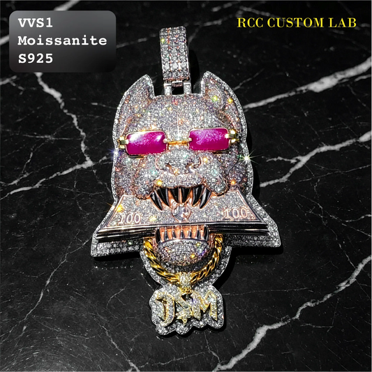 A custom cat-shaped pendant heavily encrusted with clear stones, featuring pink moissanite sunglasses, gold-toned teeth, and a gold chain detail, displayed on a black marble background with 'VVS1 Moissanite S925' and 'RCC CUSTOM LAB' text overlays.