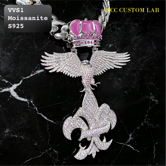 A custom pendant featuring a silver-toned phoenix with wings spread, adorned with pavé crystals and a vibrant pink moissanite crown. The pendant is set against a black marble background with white veining, featuring text overlays 'VVS1 Moissanite S925' and 'PCC CUSTOM LAB'.