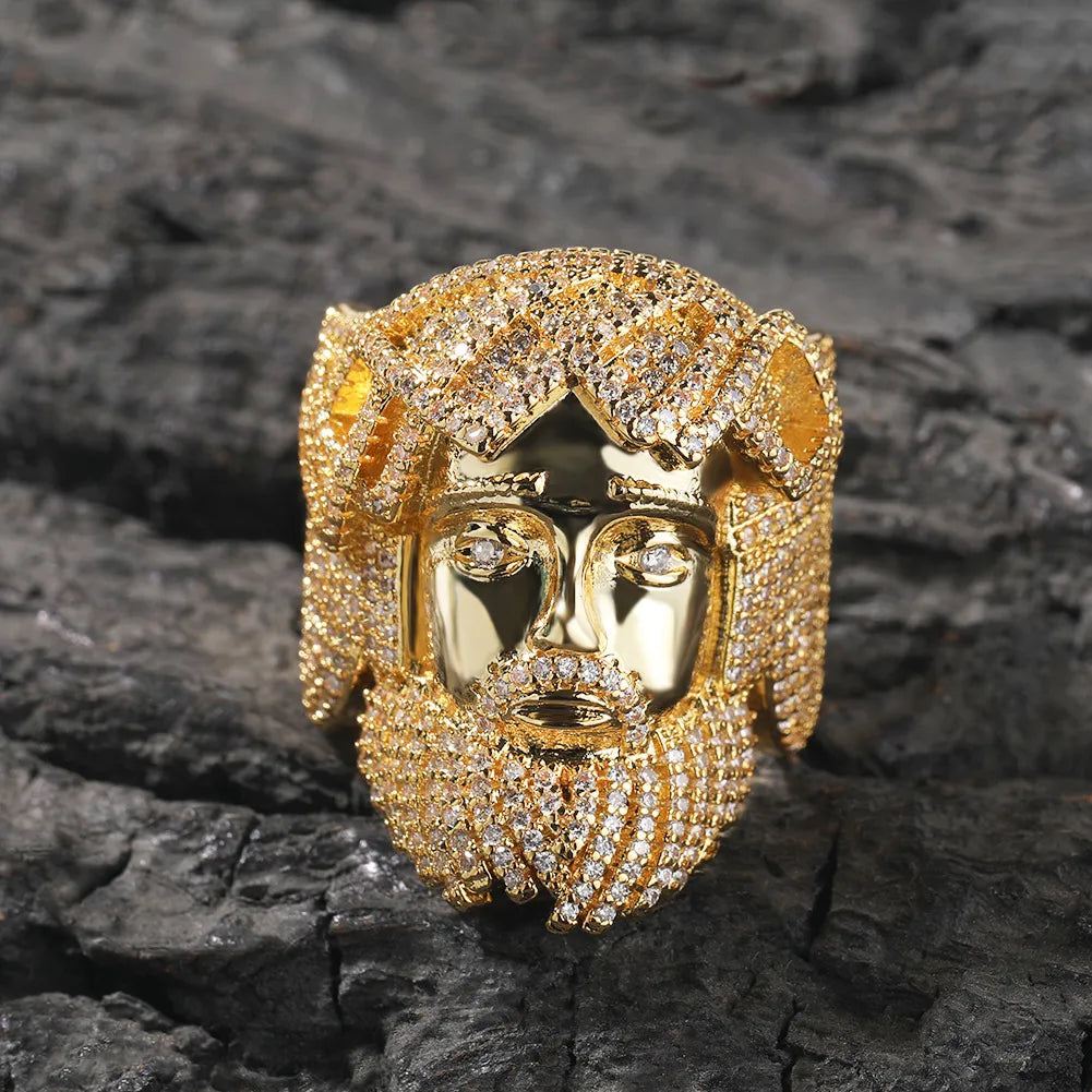 Yellow gold plated 3D Jesus head ring covered with micro pave moissanite stones, realistic sculpted facial design, mens icy hip hop ring on rough dark charred rock surface