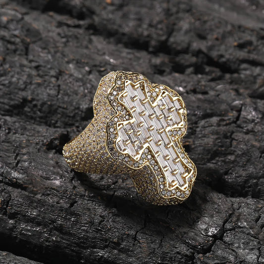 Yellow gold plated men's cross ring with layered baguette and round micro pave moissanite stones, wavy border design, icy hip hop religious statement ring displayed on rough dark charred wood