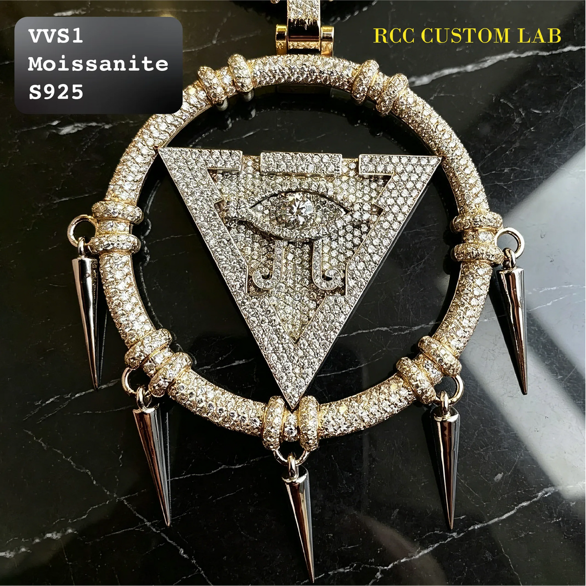 A large circular pendant with a central triangular eye motif, heavily embellished with clear stones and accented by four sharp metallic spikes. The pendant is displayed on a black marble surface with text overlays reading 'VVS1 Moissanite S925' and 'RCC CUSTOM LAB'.