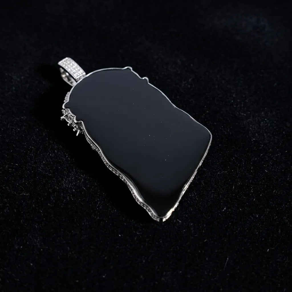 Back view of iced out Jesus pendant with smooth black enamel backing and stone paved bail, polished silver edge on dark fabric background