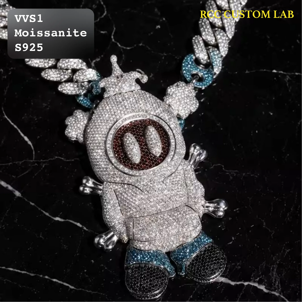 A custom Moissanite baby doll pendant necklace on a black marble background. The pendant is heavily paved with clear Moissanite, featuring a brown circular face with two white oval eyes, blue glittery pants, and a silver chain with blue and silver links.