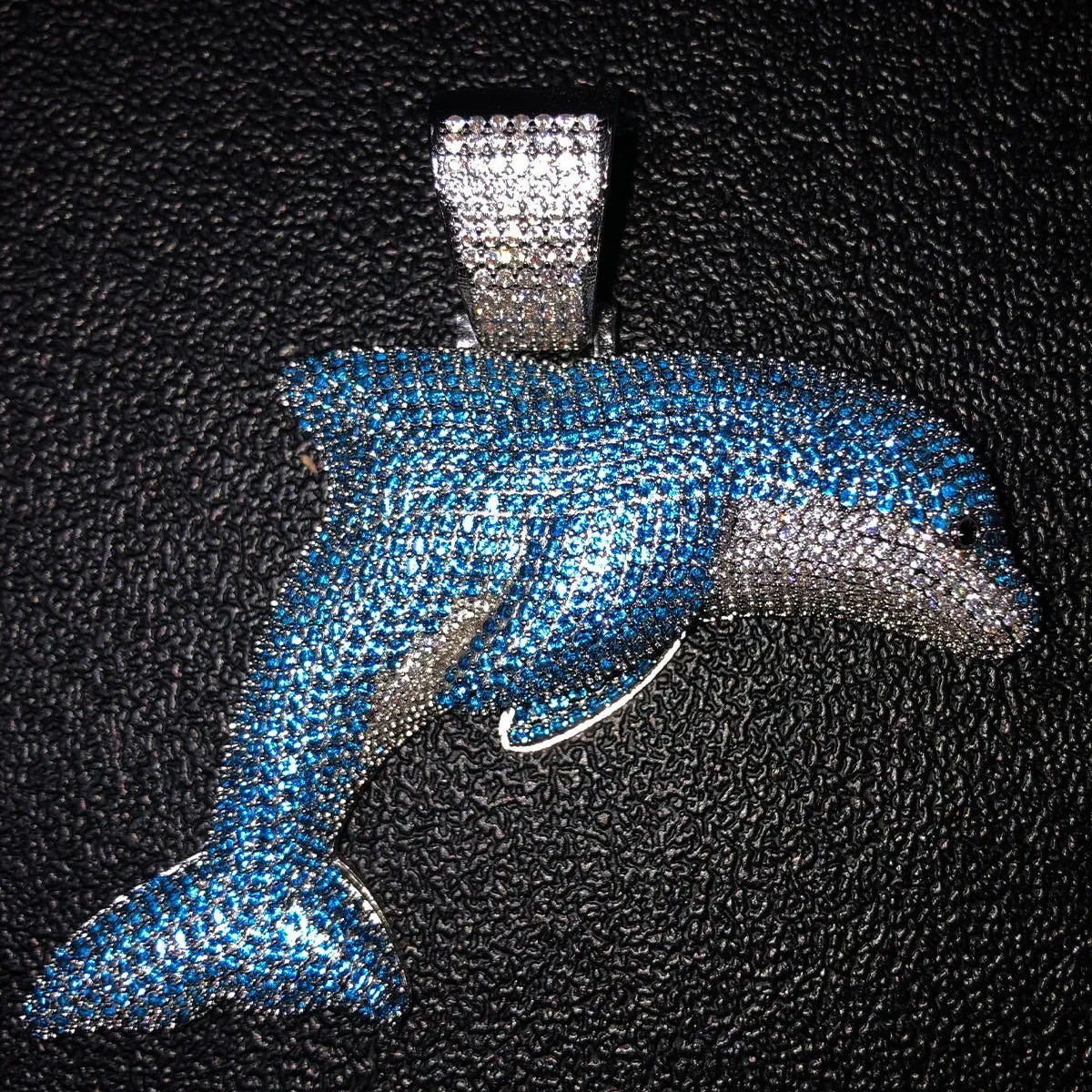 Full profile view of 3D jumping dolphin pendant fully paved with blue and white VVS1 moissanite on textured black surface.