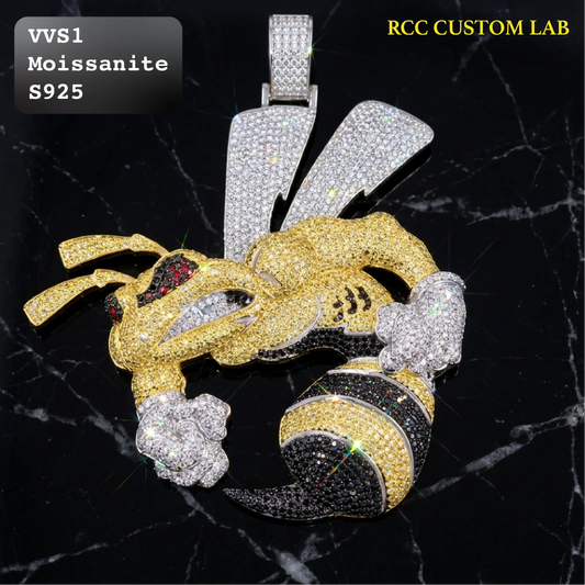 A large bee-shaped pendant covered in sparkling stones, shown on a black marble background. The pendant features a gold body, silver wings, and black-and-gold striped legs, with text overlays reading 'VVS1 Moissanite S925' and 'RCC CUSTOM LAB'.