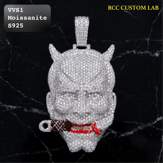 A custom pendant featuring a devil mask design, heavily encrusted with clear stones and accented with red enamel around the mouth, shown on a black marble background. Text overlays read 'VVS1 Moissanite S925' and 'RCC CUSTOM LAB'.