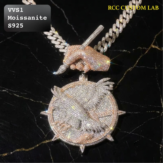 A heavily embellished necklace pendant and chain set with sparkling clear stones on a black marble background. The pendant features a circular design with a hand holding a sword, and the chain is a thick Cuban link style.