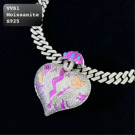 A heart-shaped pendant necklace featuring a silver-toned pavé setting with purple and pink moissanite inlay, suspended from a silver Cuban link chain on a black background. A text overlay in the top-left corner reads 'VVS1 Moissanite S925'.