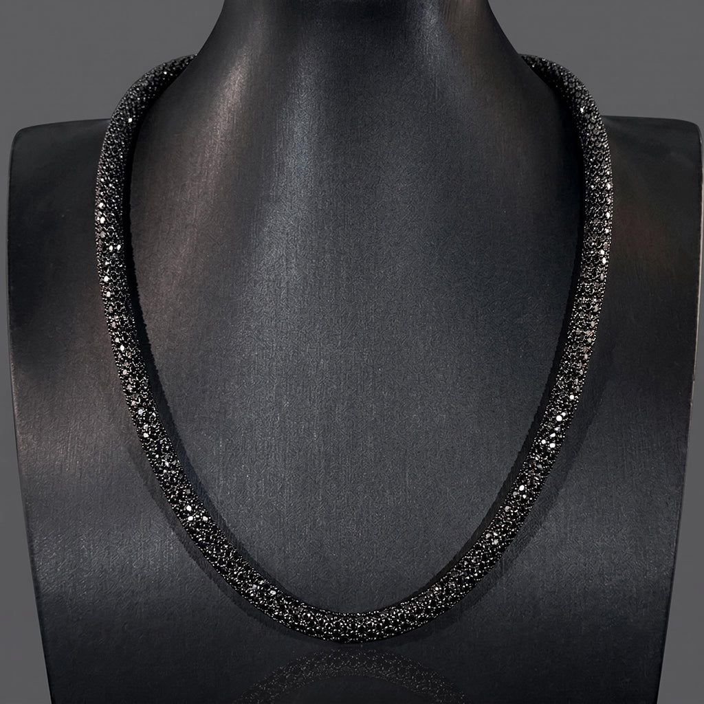 A black beaded necklace displayed on a dark gray mannequin bust against a dark gray background.
