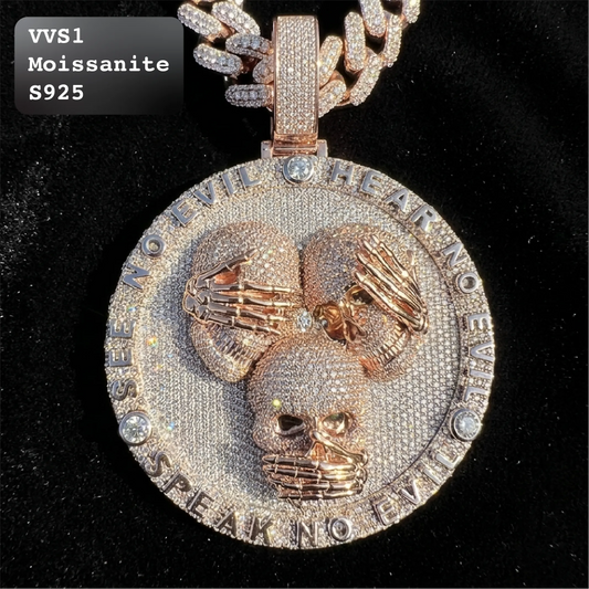 A close-up of a large round pendant necklace on a black background. The pendant is rose gold-toned and heavily paved with clear stones, featuring three skulls with skeletal hands over their eyes, mouth, and nose.