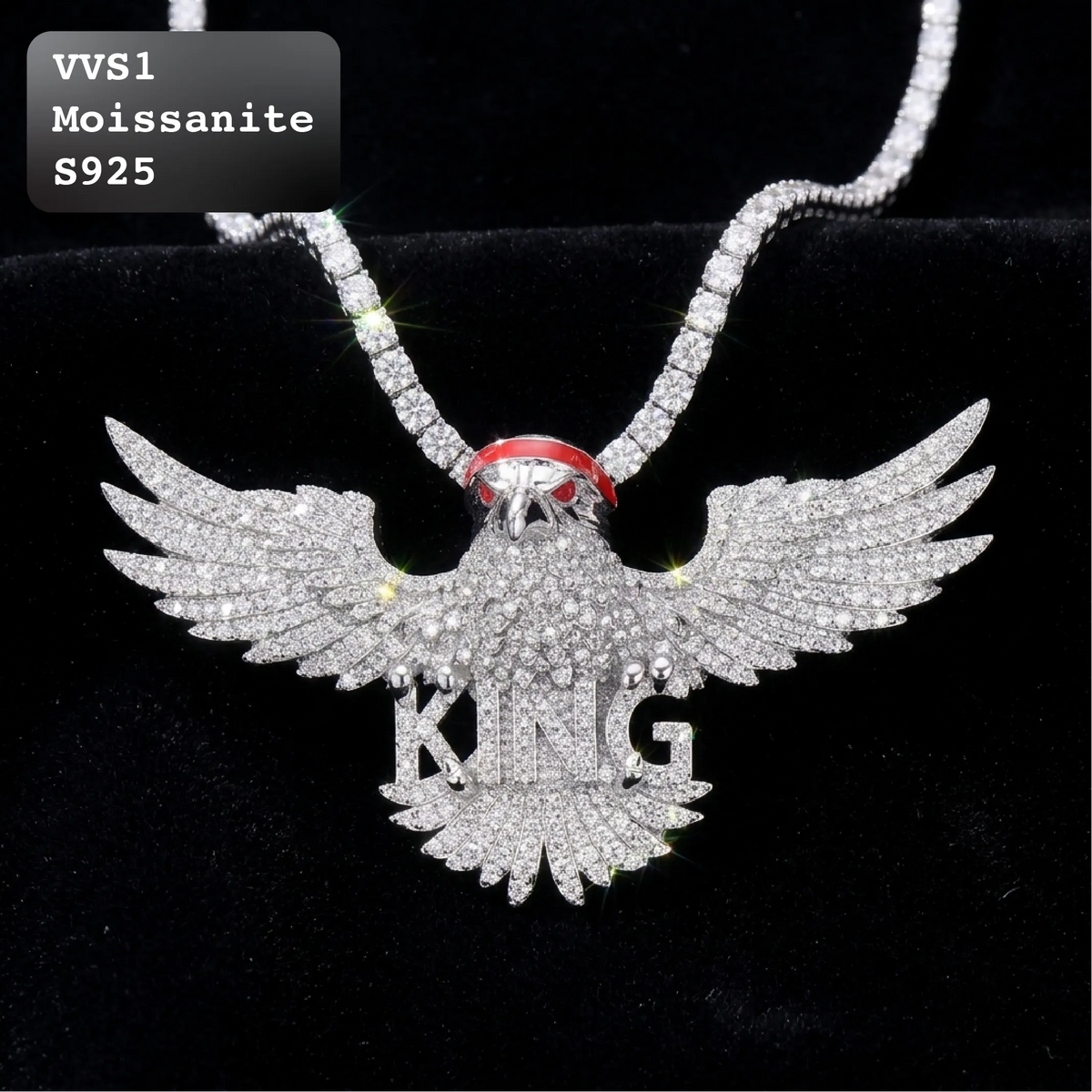 A silver-toned moissanite eagle pendant necklace with 'KING' spelled out in the wings, displayed on a black velvet background. A red gemstone accent is visible at the neck of the pendant.