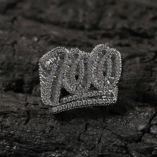 Silver micro pave moissanite "100" numeric hip hop ring with baguette cut stones, displayed on rough dark charred bark texture