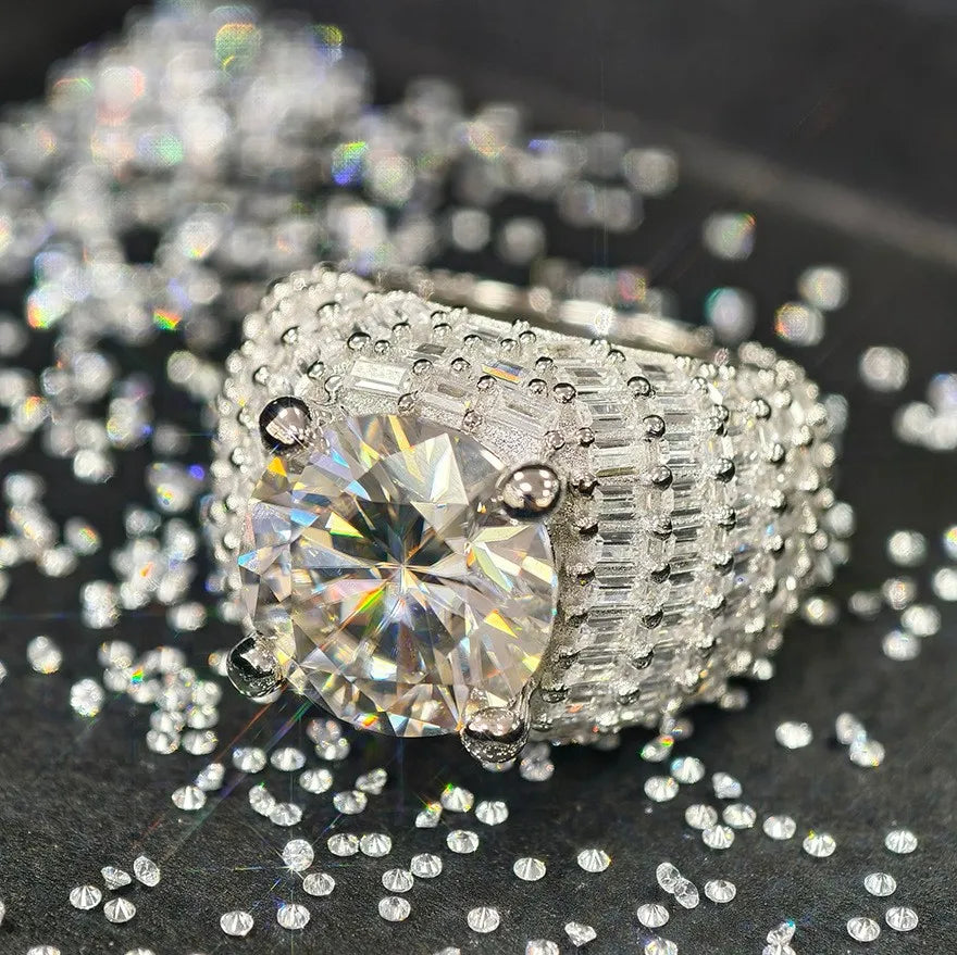 Oversized silver men statement ring with massive round moissanite center stone, full baguette paved wide band, laid among scattered loose moissanite stones, premium hip hop icy jewelry