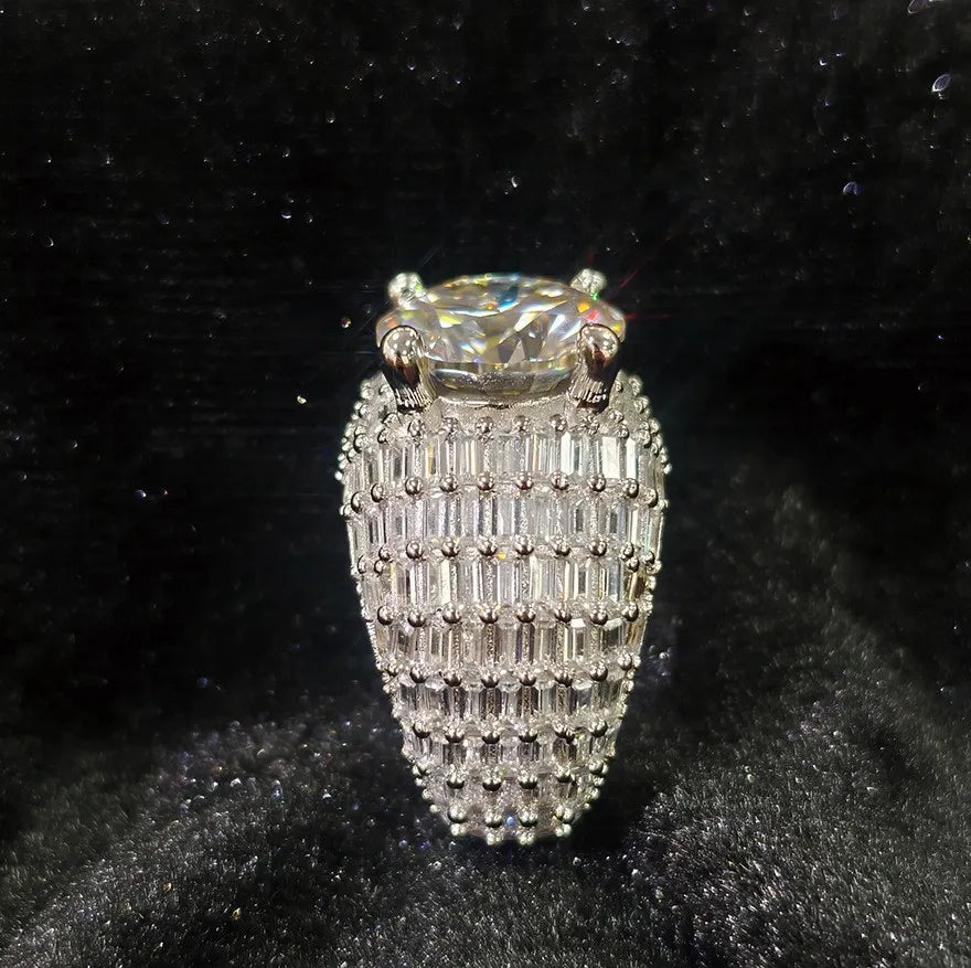 Front vertical view of silver men tall dome shaped moissanite ring, large round center stone, densely set baguette stones covering wide band, bold hip hop bling ring on dark velvet background