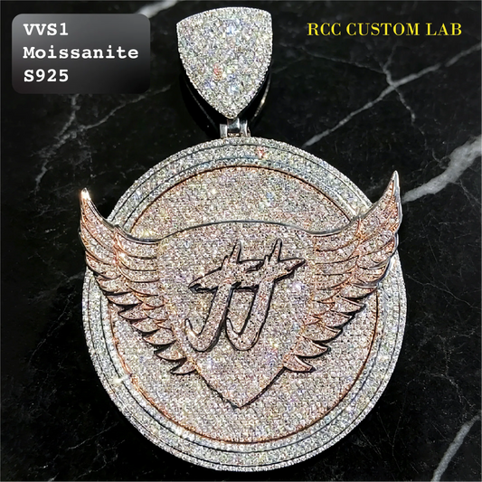 A large round pendant with a shield and wing design, heavily paved with sparkling stones. The center features an engraved monogram logo.