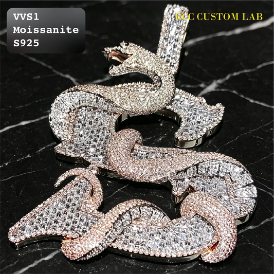 A coiled snake pendant covered in sparkling stones, shown on a black marble background. The top left corner has a label reading 'VVS1 Moissanite S925' and the top right corner has 'RCC CUSTOM LAB' text.