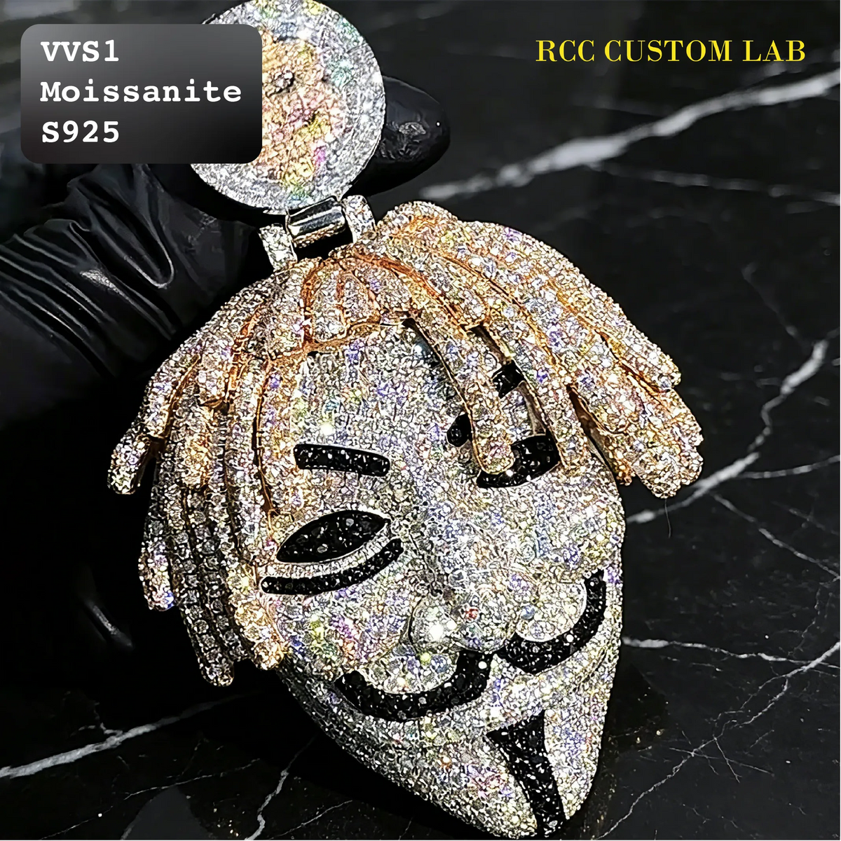 A large, highly detailed pendant shaped like a stylized face with braided hair, covered in sparkling rhinestones and black rhinestone accents, held by a black gloved hand against a black marble background. Text overlays read 'VVS1 Moissanite S925' and 'RCC CUSTOM LAB'.